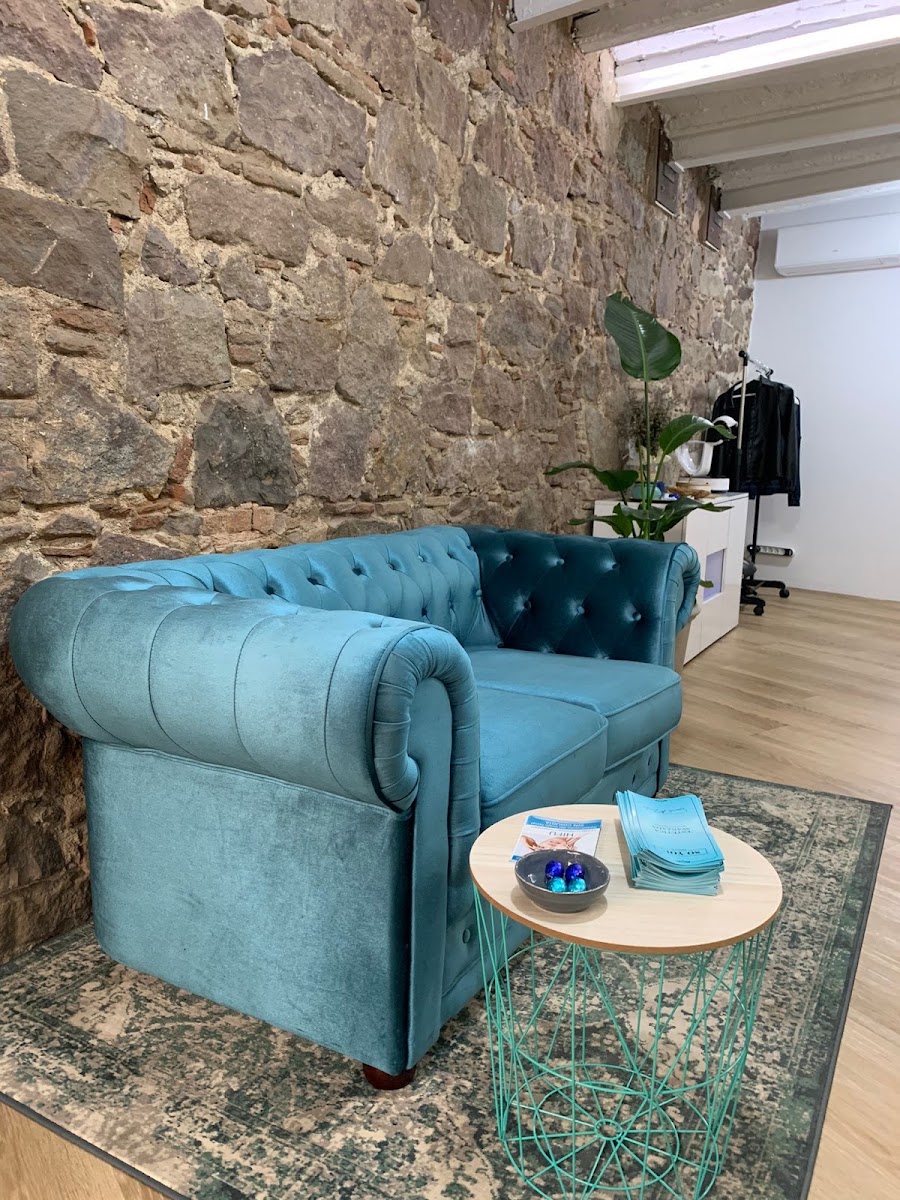 Sala de espera con sofá azul estilo chesterfield, mesa auxiliar turquesa y pared de piedra