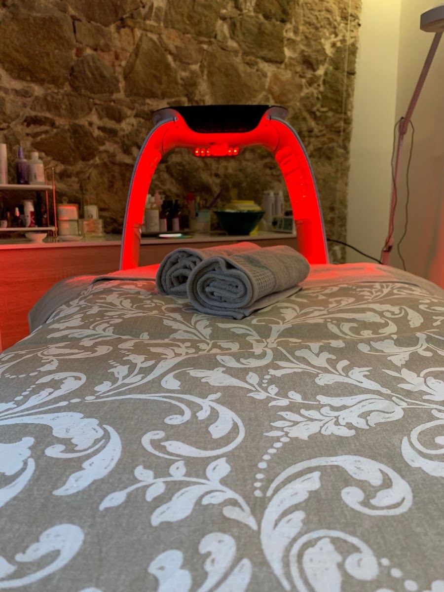 Camilla de tratamiento con arco de luz LED roja y toallas grises sobre pared de piedra