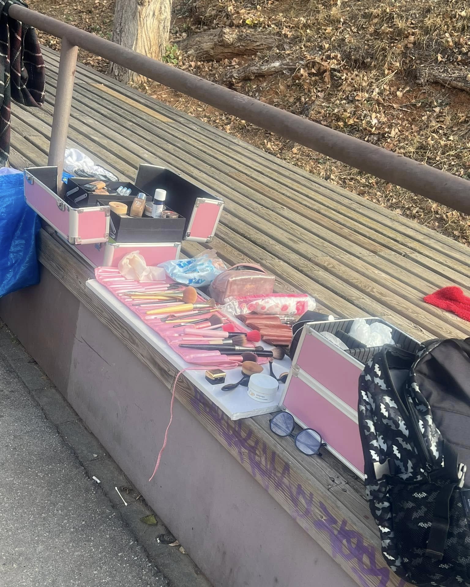 Productos de maquillaje y herramientas organizados sobre un banco de madera en exteriores